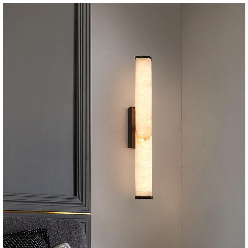 Alabaster stone cylinder aerq sconce mounted on a dark grey panelled wall in a modern bedroom