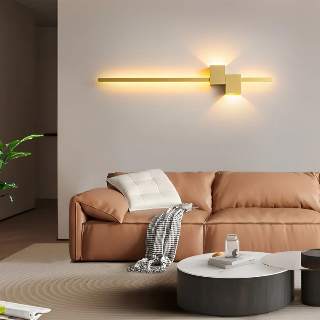 Gold horizontal linear aexi LED wall lamp mounted above a tan leather sofa in a stylish living space