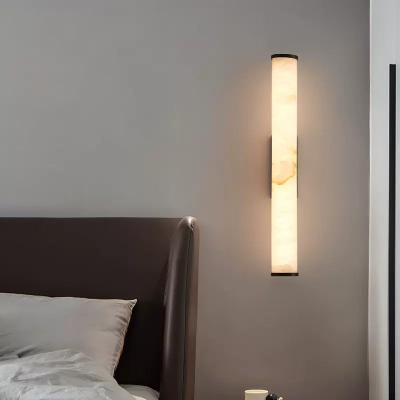 Alabaster stone wall light acting as a luxurious ambient bedside lamp next to a dark headboard