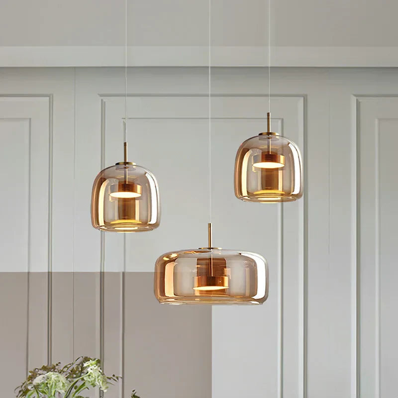Cluster of three amber glass pendant lights in various shapes suspended over a modern dining table