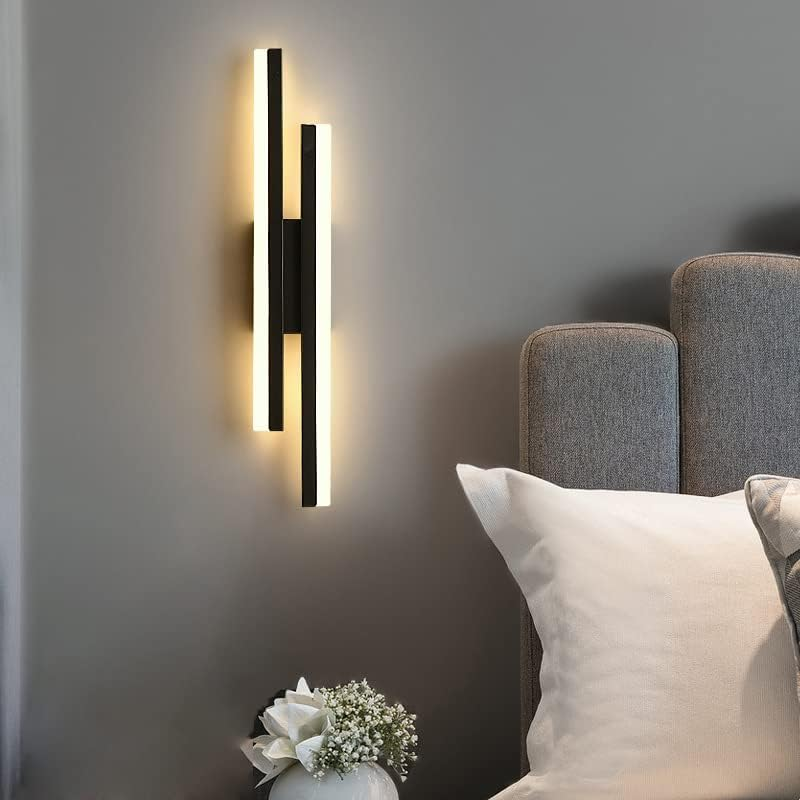 Asymmetrical black linear LED sconce illuminating the wall next to a modern grey tufted headboard