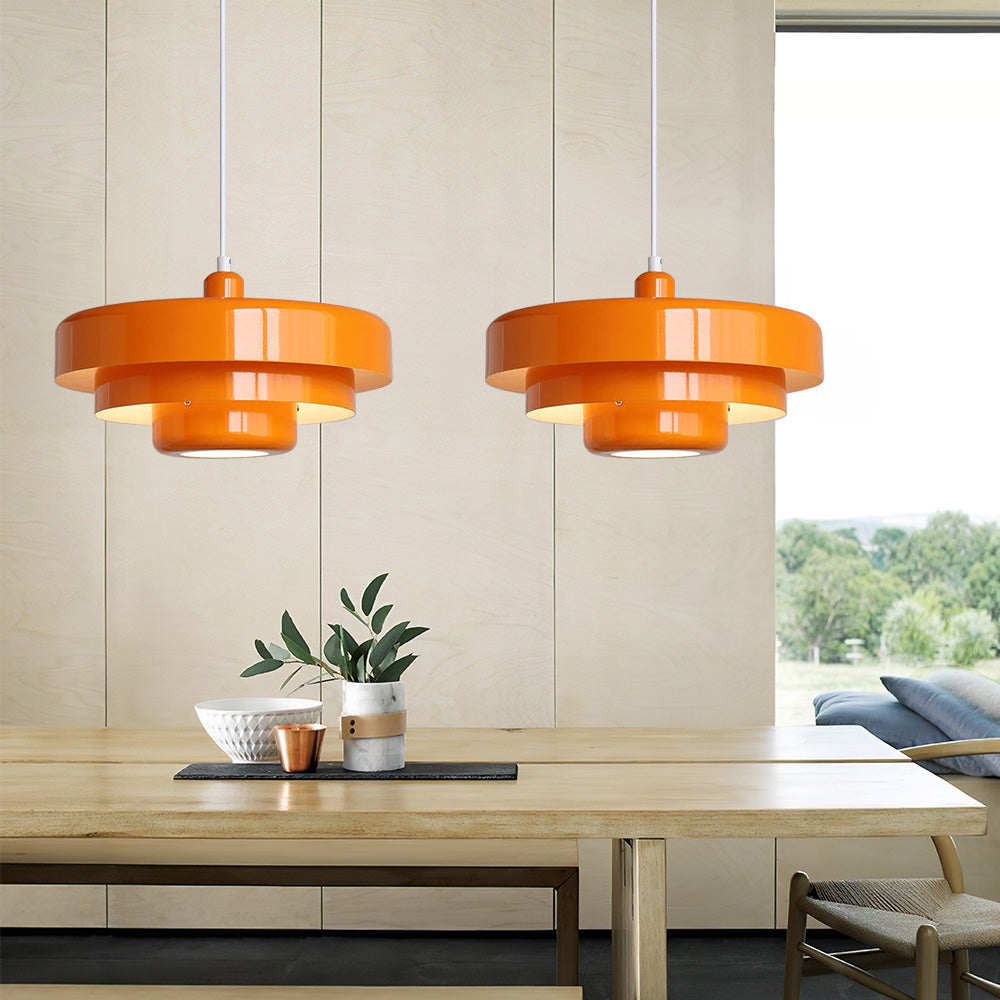 Two retro balel orange Bauhaus pendant lights hanging over a large dining table in a bright, sunlit room