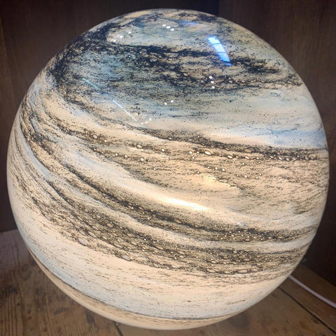 Close-up detail of the glowing beige and brown planetary glass sphere, highlighting its intricate swirling surface pattern