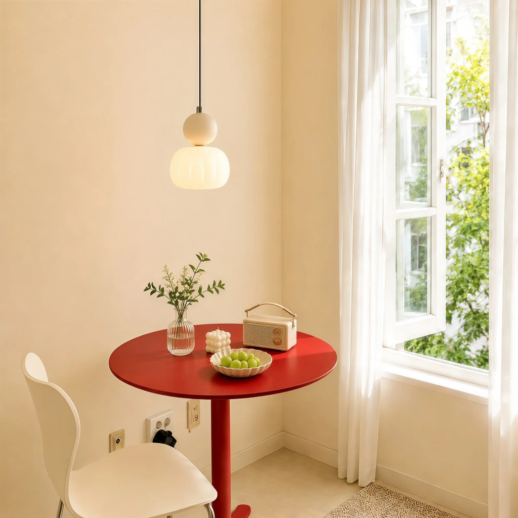 Beige geometric pendant light suspended over a small red dining table in a sunlit corner