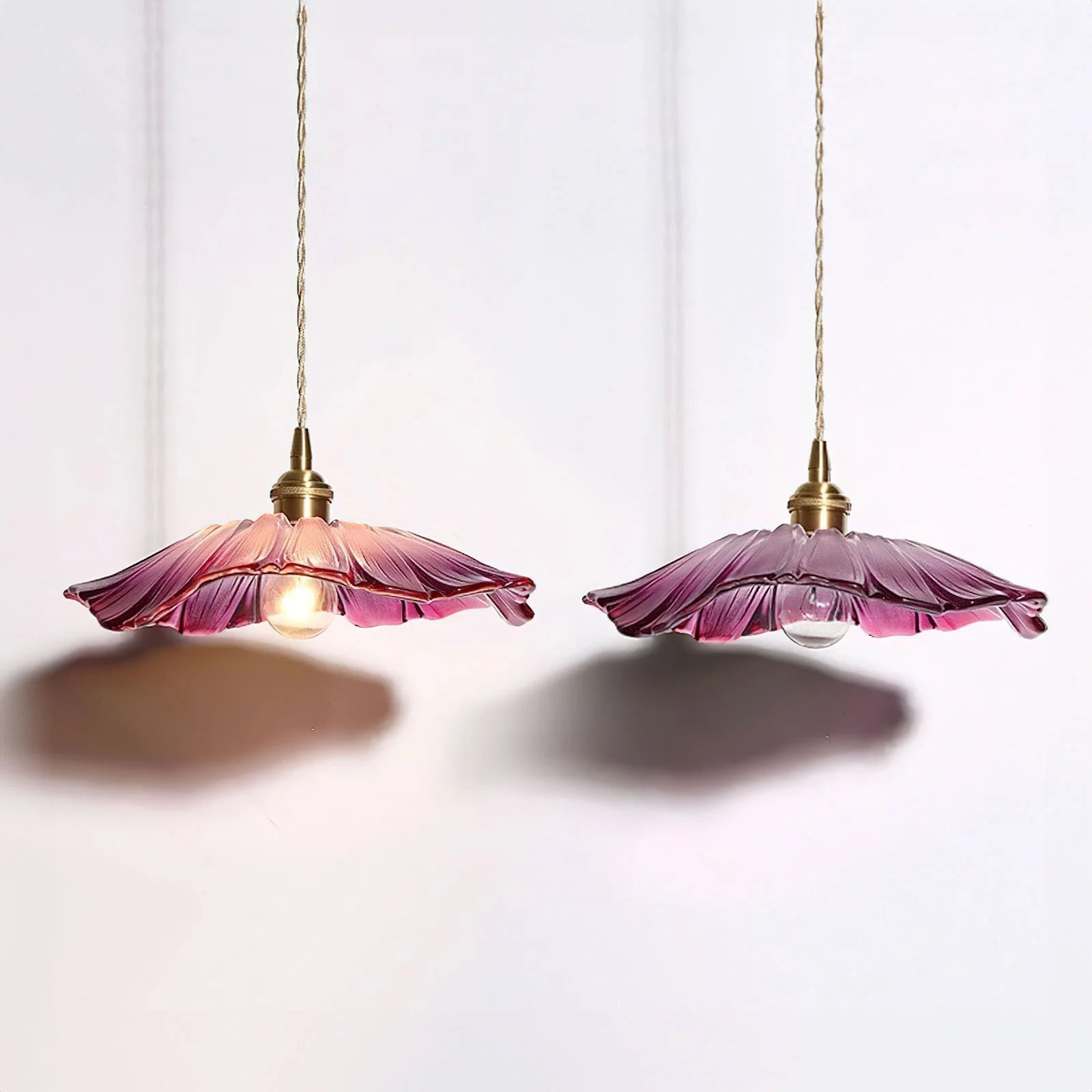 Pair of purple lotus bila glass pendant lights casting a warm, colourful glow against a white wall