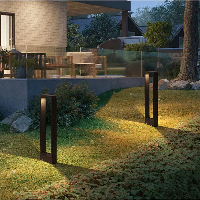Black architectural LED path lights lighting up a grassy slope near a modern outdoor patio