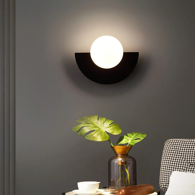 Black minimalist globe wall light casting a soft, glare-free ambient glow over a decorated side table