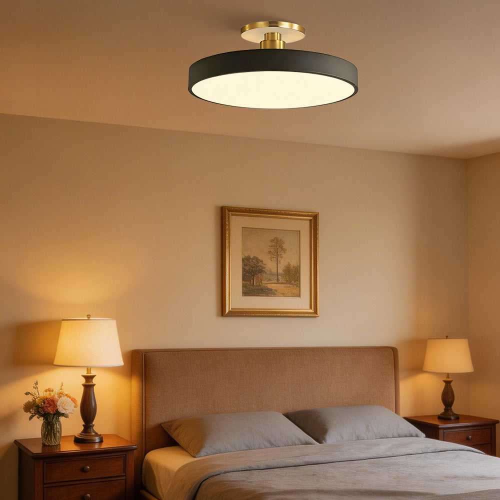 Black round LED semi-flush mount casting a warm ambient glow in a cosy bedroom setting