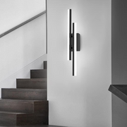 Modern black staggered linear LED wall sconce installed vertically next to a contemporary wooden staircase