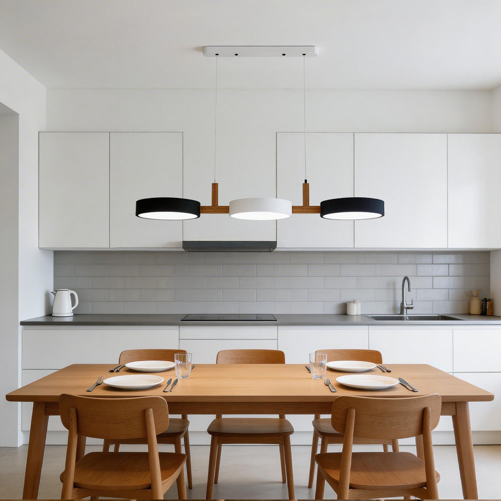Black, white, and black 3-head pendant illuminating a long wooden dining table in a minimalist kitchen