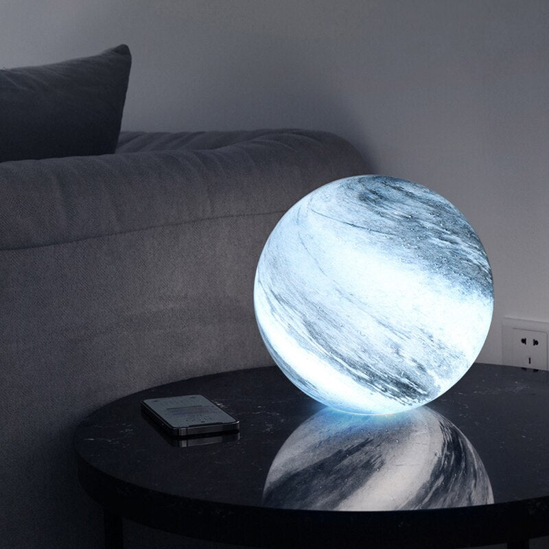 Blue planetary globe lamp casting a soft ambient light on a dark glass living room table