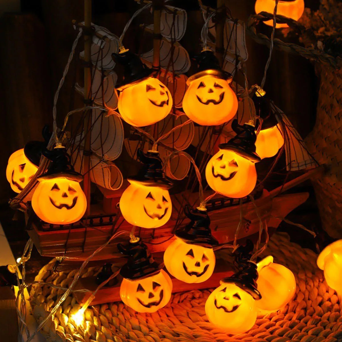 Close-up of glowing Brimsparks pumpkin-shaped LED string lights beside a decorative model ship