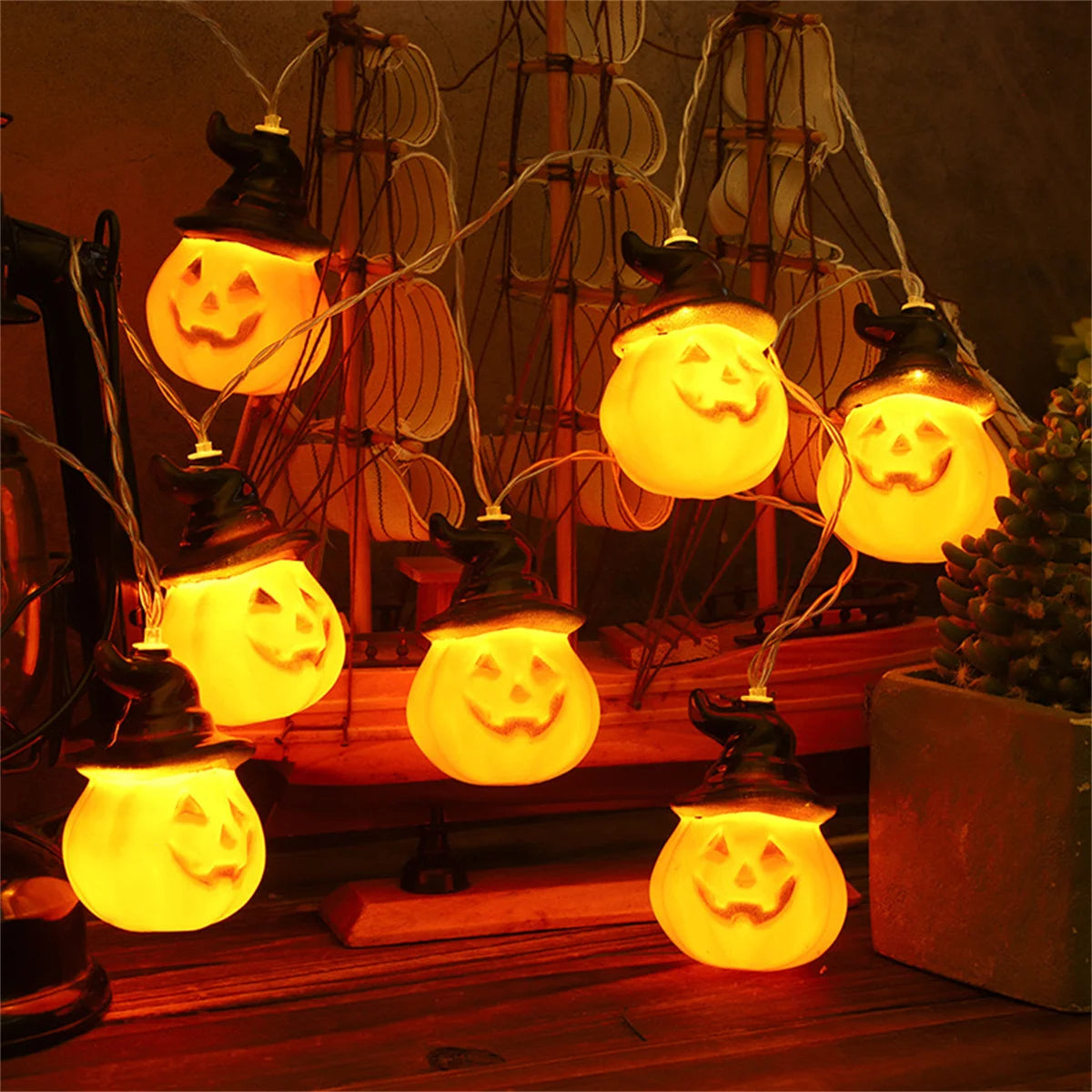 Brimsparks pumpkin-shaped LED string lights glowing around a decorative model ship and potted plant
