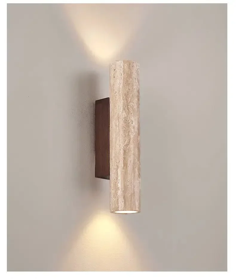 Modern cylindrical travertine bura wall sconce casting a warm up and down light on a plain wall