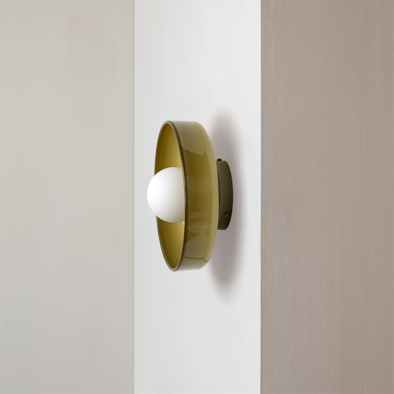 Olive green glass disc cenas wall light with a milky-white opal globe mounted on a white wall