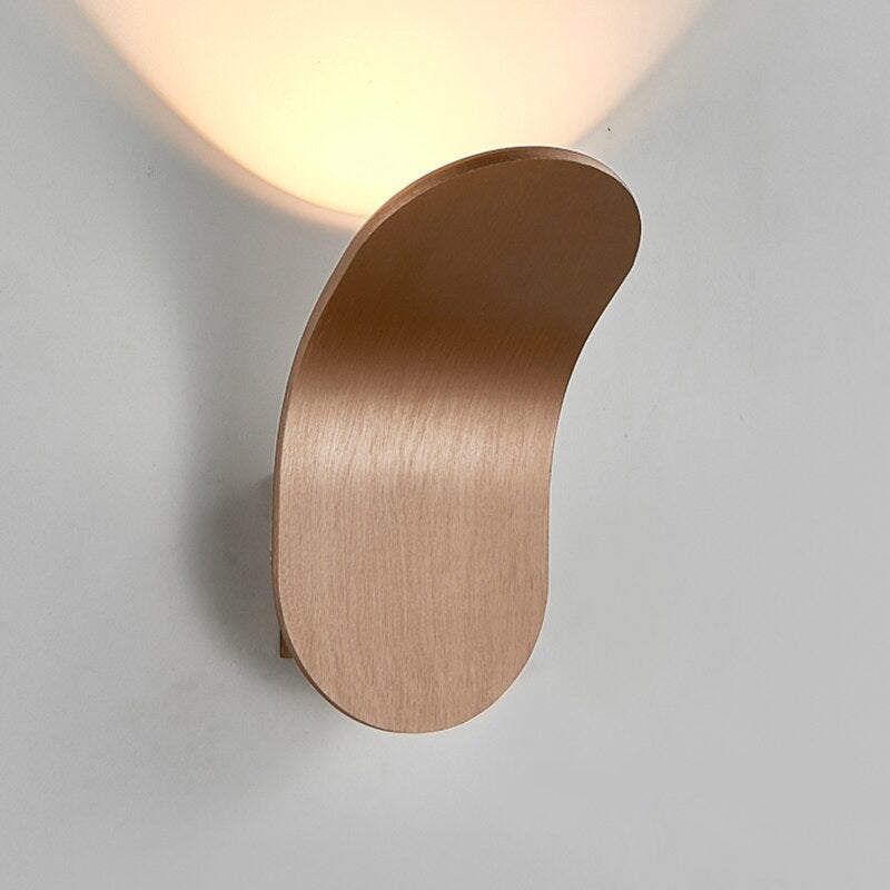Champagne coloured curved LED sconce glowing warmly against a light grey wall