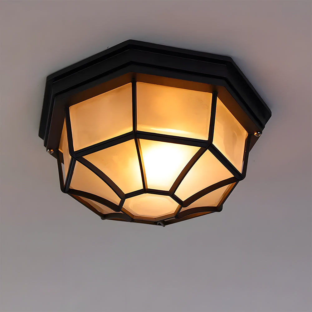 Close-up of an illuminated black rustic bulkhead lamp featuring a protective metal cage and frosted glass