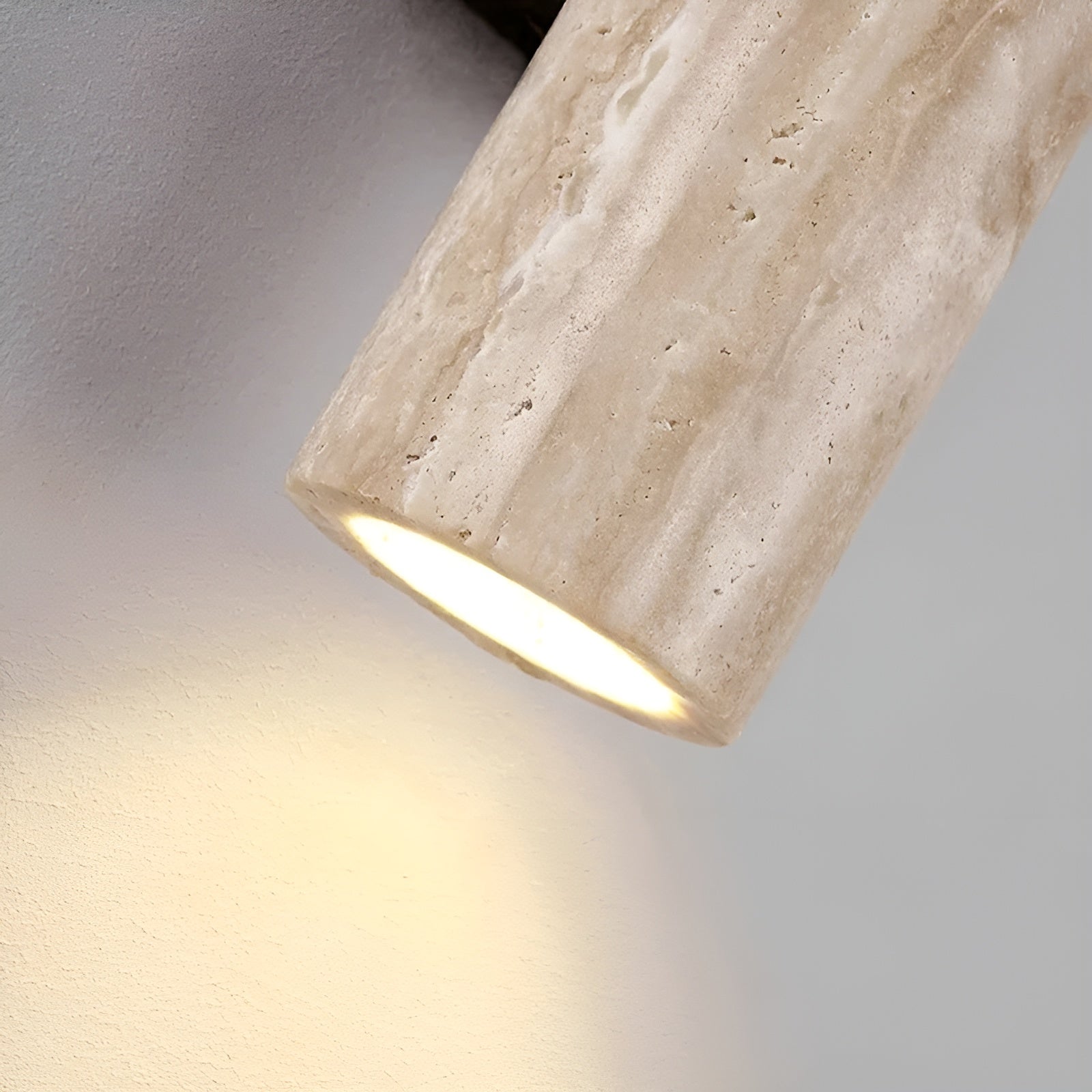 Close-up detail of the natural travertine wall sconce showing the warm LED light emitting from the bottom