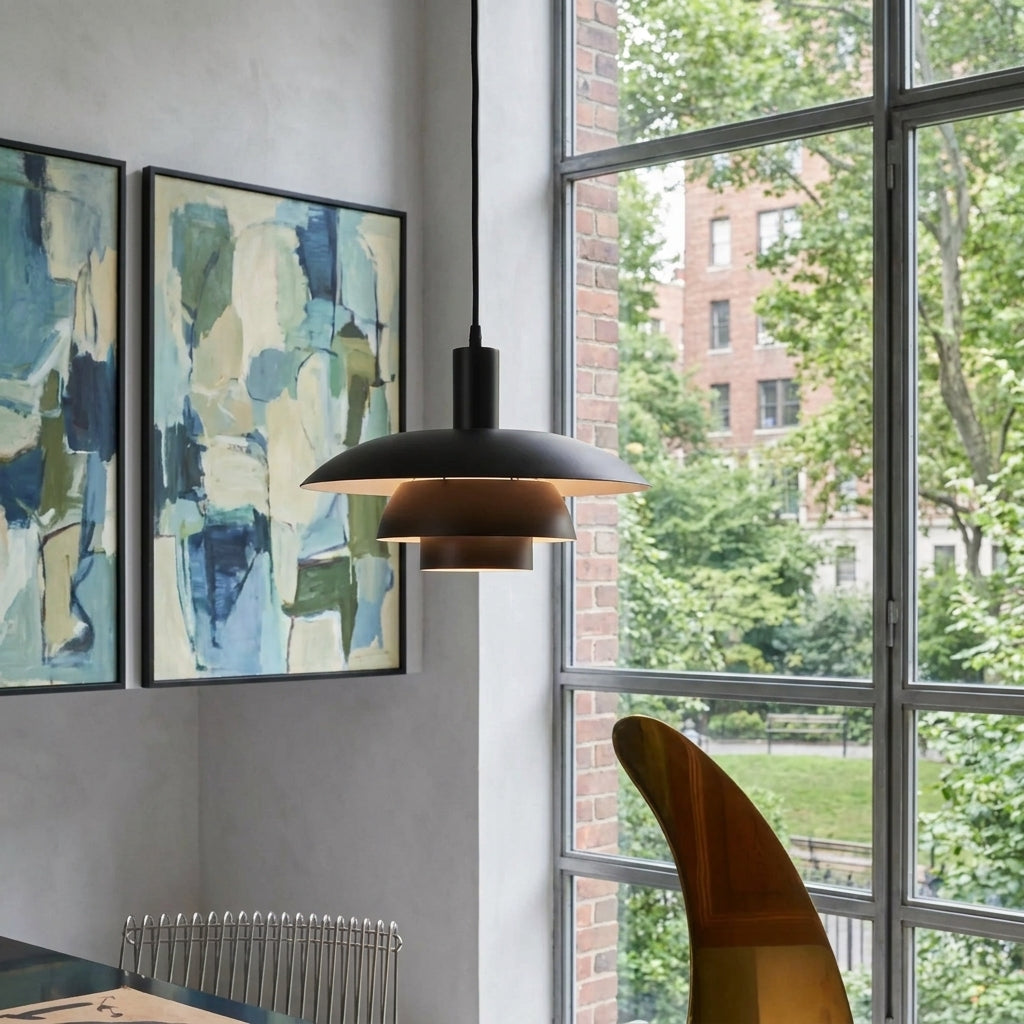 A modern black pendant light hangs in a stylish room next to a large window with an outdoor view, with abstract wall art and a wooden chair visible.