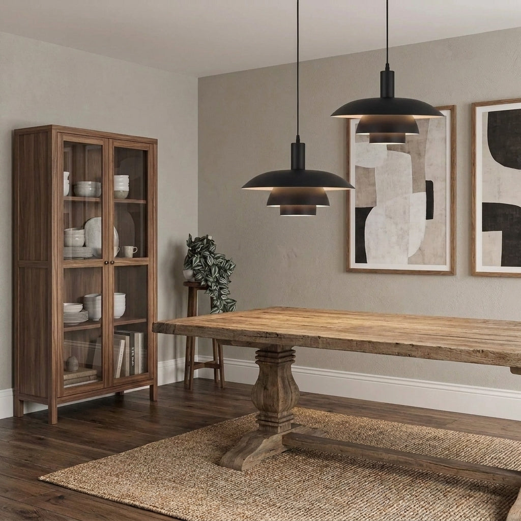 A rustic wooden dining table with a thick natural wood top and turned pedestal legs, set on a woven jute rug in a dining room. Two black pendant lights hang above, and a tall wooden cabinet and framed abstract wall art are visible in the background.
