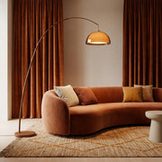 Dalzi mid-century arc floor lamp with walnut-finish arm and amber dome shade over a curved terracotta sofa