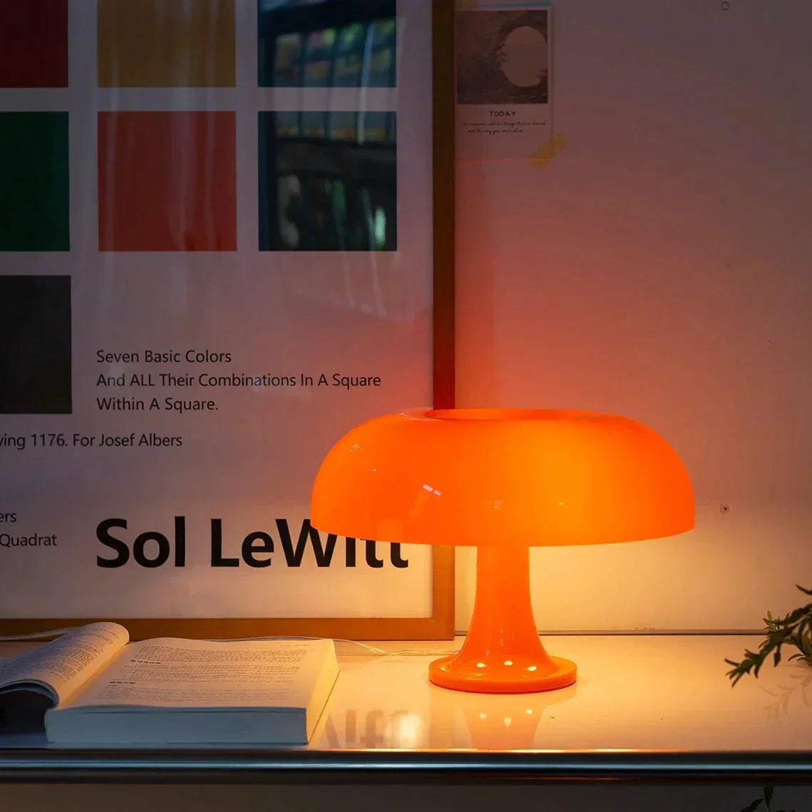 Vibrant orange retro mushroom euter table lamp illuminating a modern desk next to an open book and framed poster