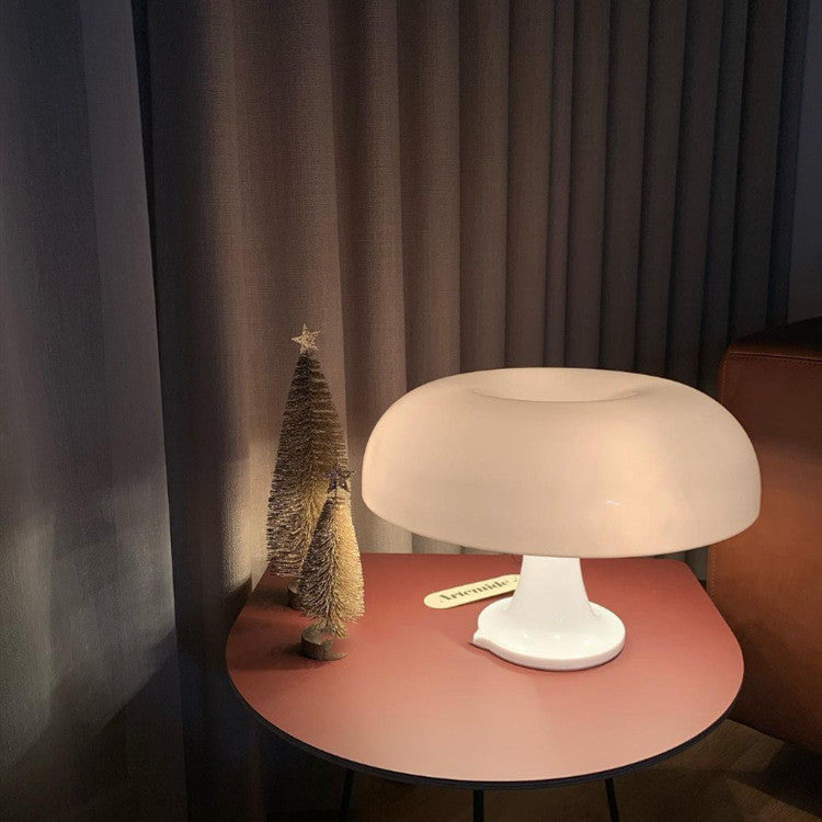 White mid-century modern mushroom euter nightlight casting a warm glow on a round red bedside table