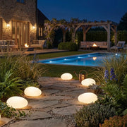 Fexil solar pebble lights lining a stone path around a pool and garden at night