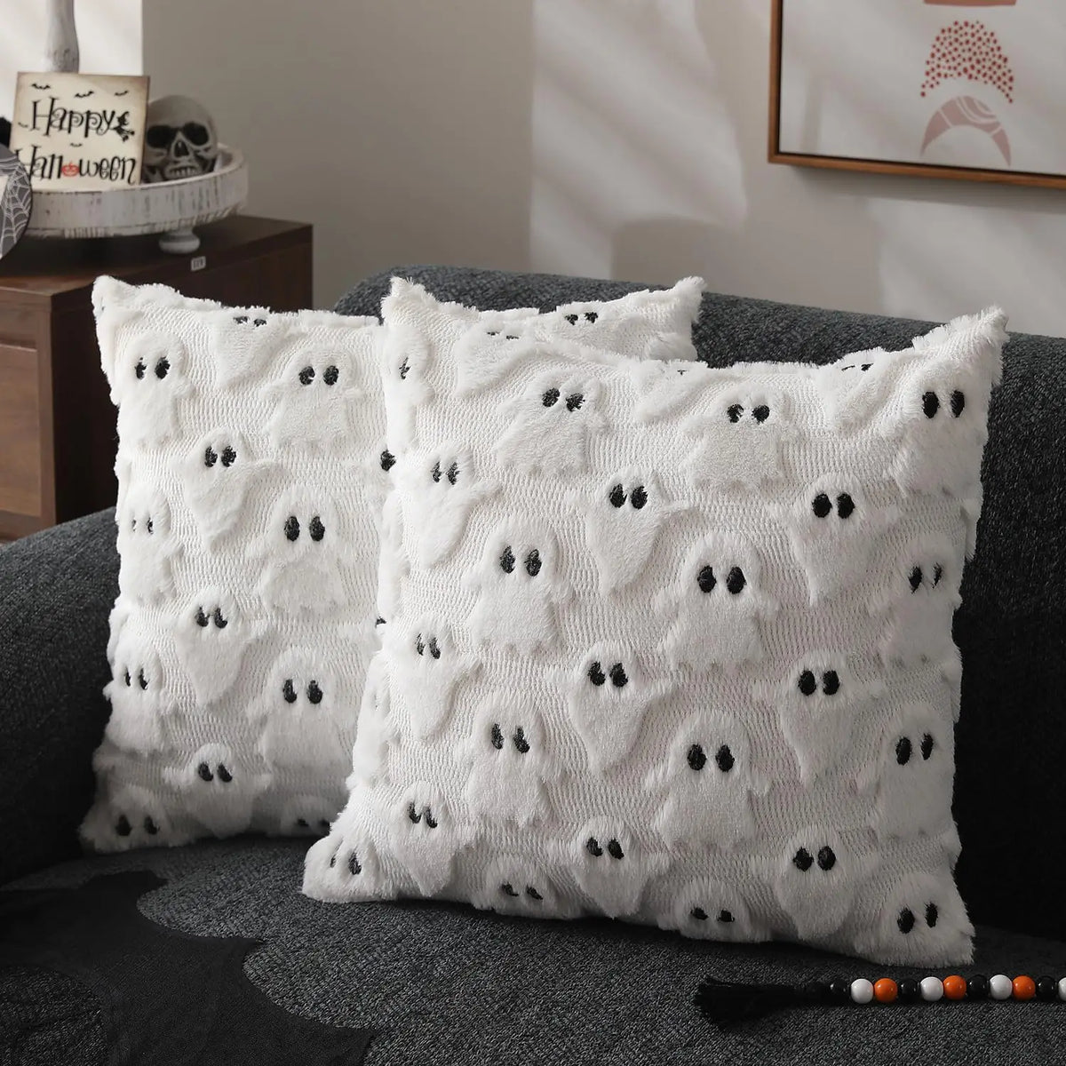 White all-over ghost print Halloween throw pillow covers styled on a dark grey sofa with a Happy Halloween sign