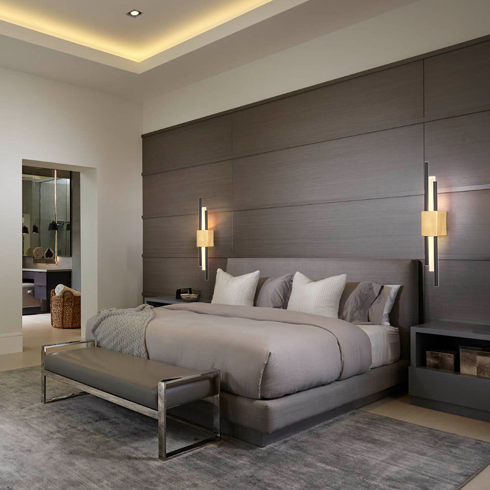 Gold staggered wall sconce illuminating a bedside table in a luxury, neutral-toned bedroom suite