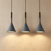 Three graphite Nordic funnel pendant lights illuminating a textured beige wall with a warm, focused glow