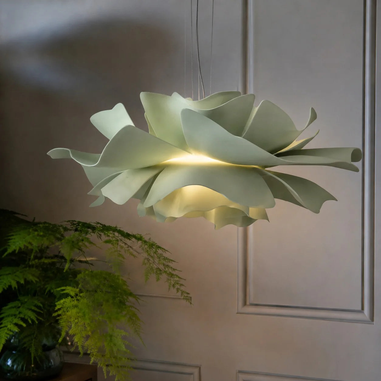 Close-up of the sage green acrylic floral pendant casting a warm glow in a botanical setting