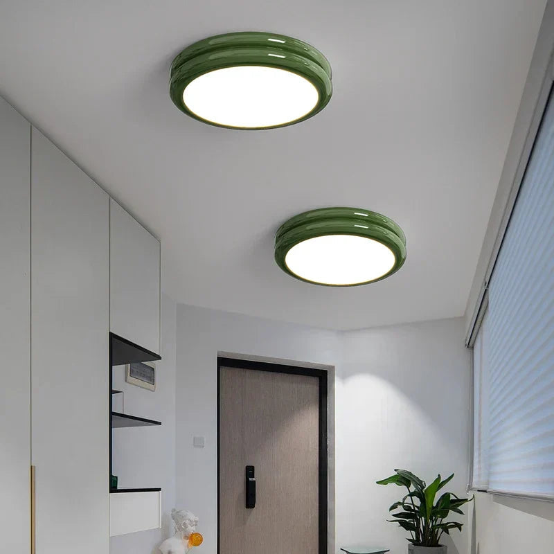 Two green glossy metal flush mount ceiling lights installed in a minimalist white entryway