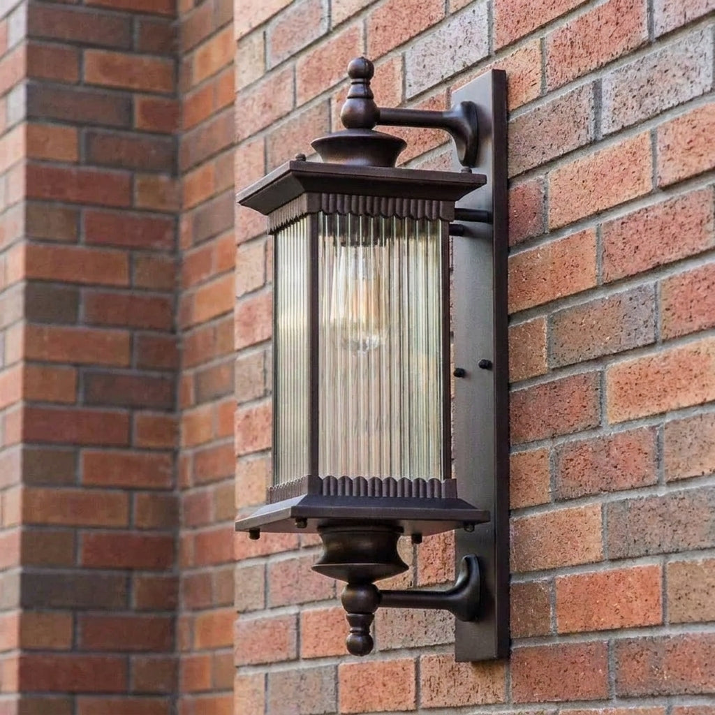 A dark brown outdoor wall sconce with a ribbed glass shade, mounted on a red brick wall.