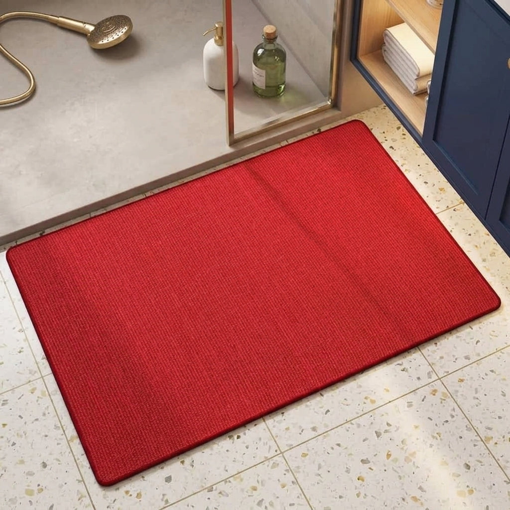 A rectangular red bath mat with a textured surface, shown on a speckled bathroom floor near a shower area.