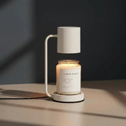 Jomzi white candle warmer lamp lit with a Flower Market scented candle on a dark desk
