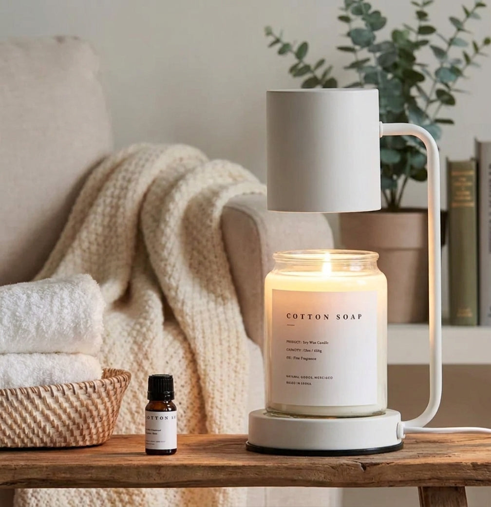 Jomzi white candle warmer lamp on a side table beside a throw blanket and fragrance oil