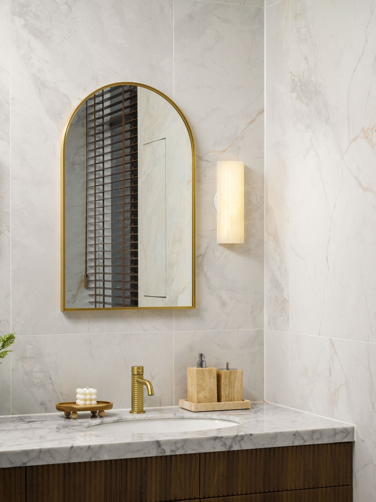 Fluted stone jopna wall sconce acting as elegant, warm lighting next to a modern bathroom vanity mirror
