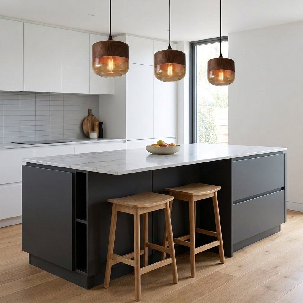 Three pendant lights hanging over a modern kitchen island with a white marble countertop and dark grey cabinetry, with two wooden bar stools in a bright kitchen setting.