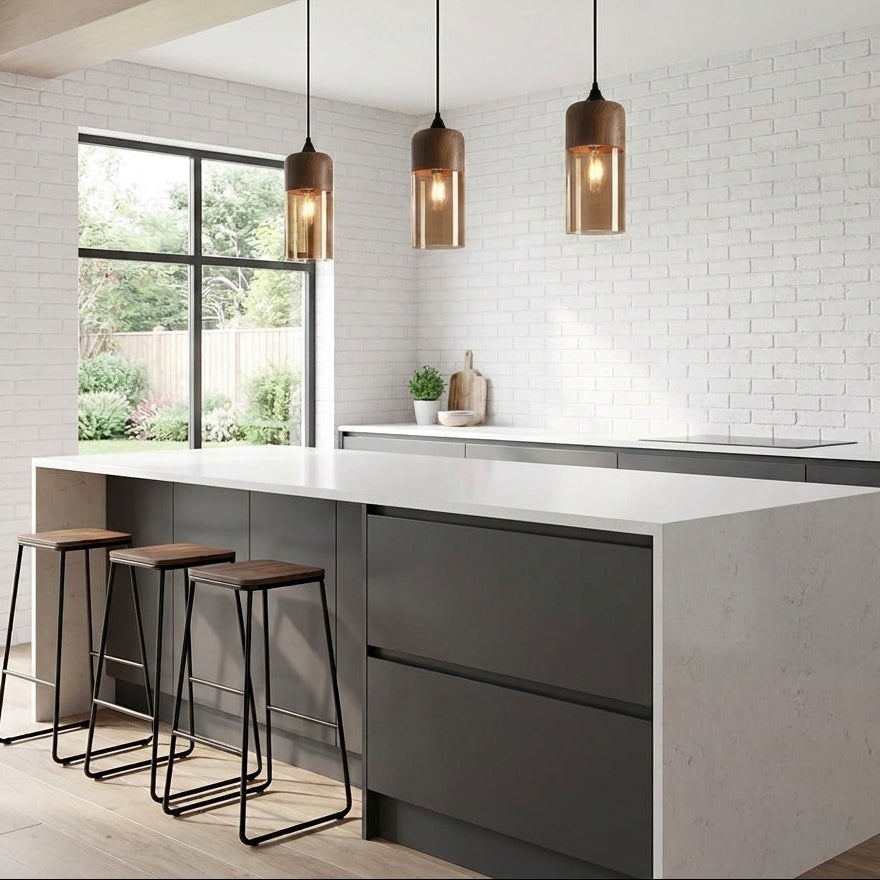 Three modern pendant lights with tinted shades and black cords hang over a white-topped kitchen island in a bright, contemporary kitchen with white brick walls and dark grey cabinetry.