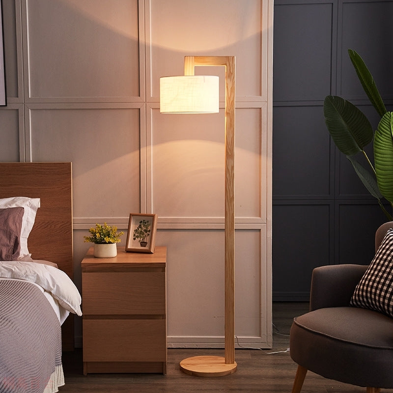 Wooden reading kelta floor lamp providing warm ambient light next to a bedside table in a cosy bedroom