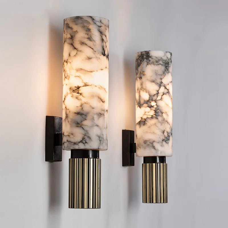 Pair of modern natural marble kopu wall sconces with fluted metallic bases glowing warmly against a white wall