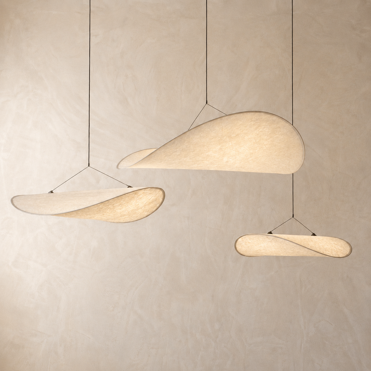 Three cascading Japanese Wabi-Sabi silk wave korta pendant lights illuminating a serene beige minimalist wall