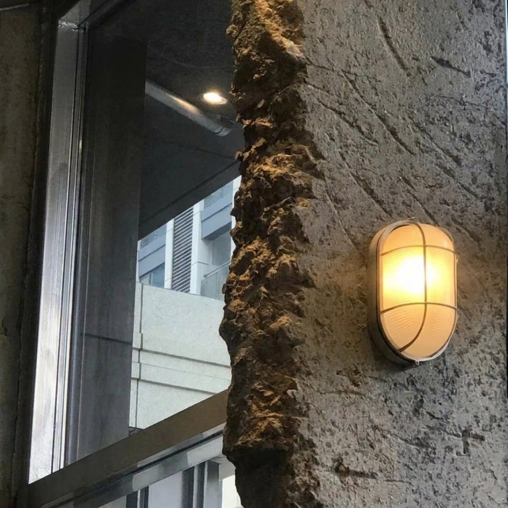 Kuxqa bulkhead wall light illuminated on an exterior stone wall at dusk