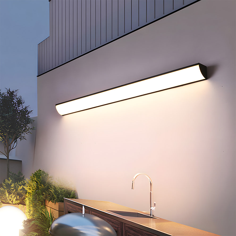 Long front-lit linear exterior sconce illuminating a modern outdoor kitchen and patio area