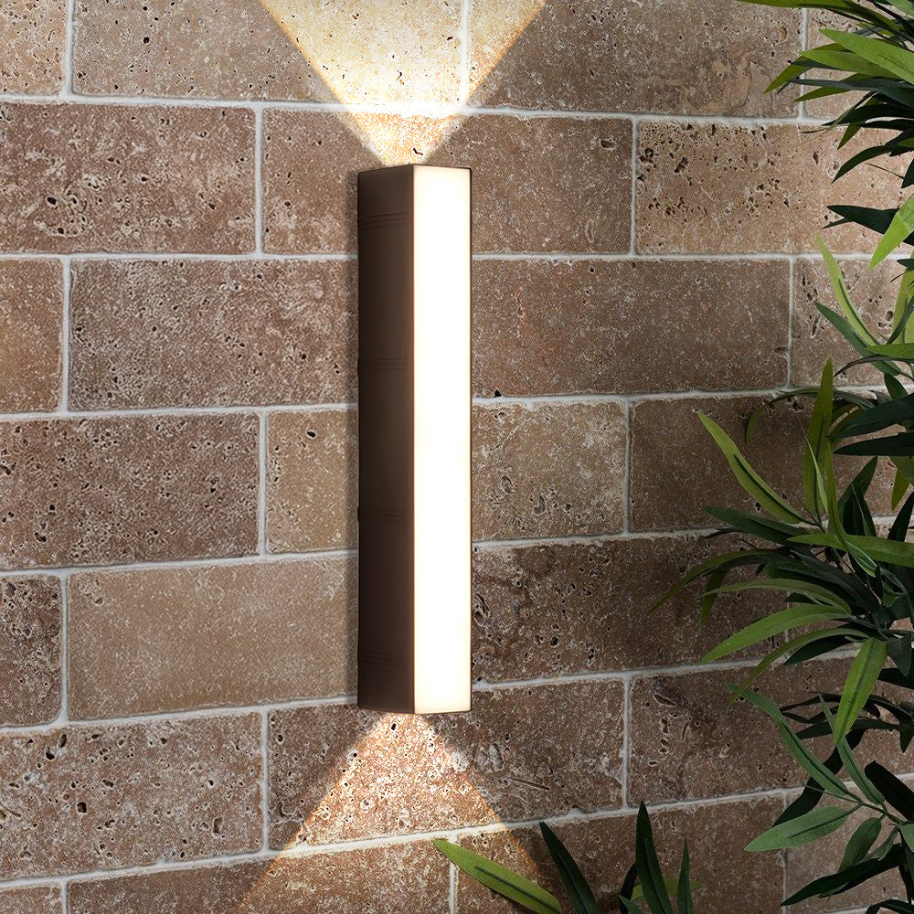 Black linear outdoor wall light installed on a textured brick facade casting a warm V-shaped glow
