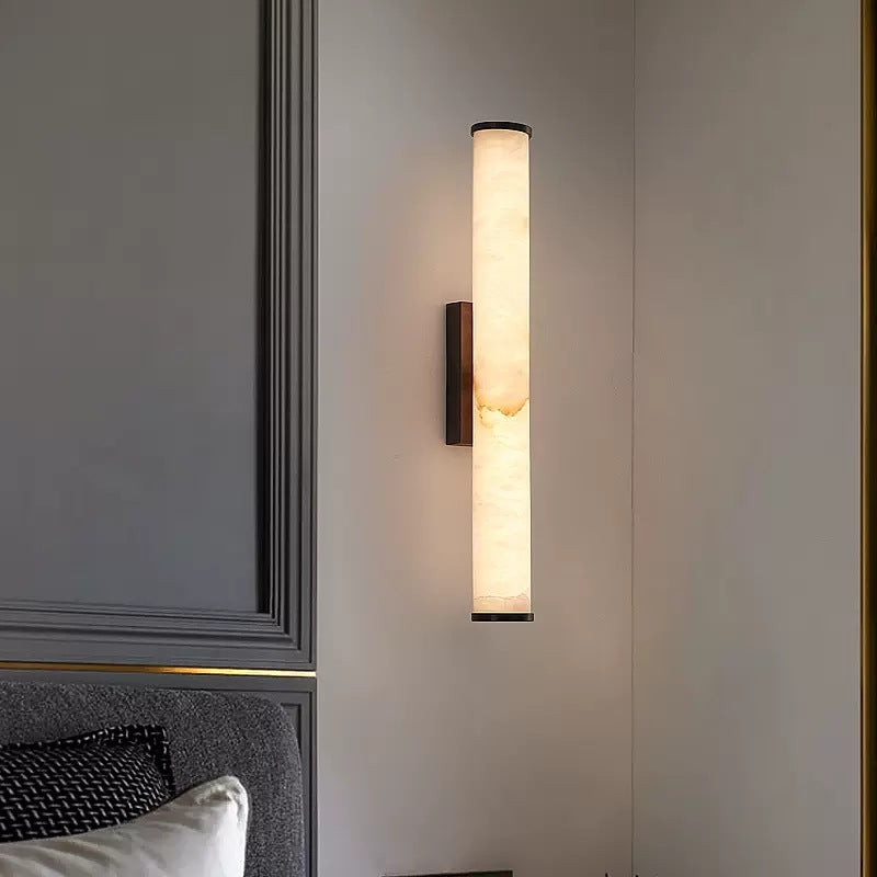 Marble tube wall sconce illuminating a contemporary bedroom with elegant grey wall panelling