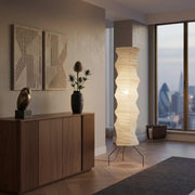 Mepzo rice paper floor lamp in a modern living room with wall art, a vase, and a city skyline view at dusk