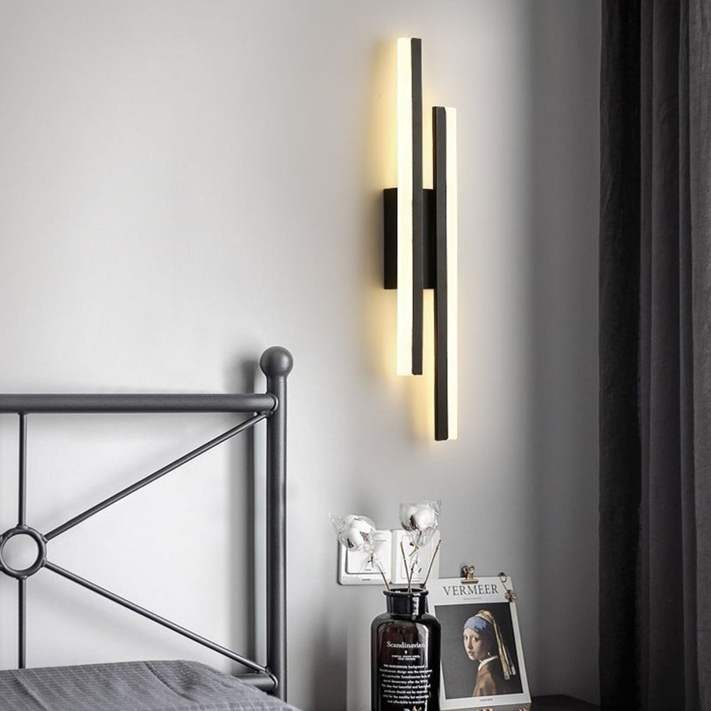 Minimalist milor linear acrylic and black metal sconce mounted next to an industrial style metal bed frame