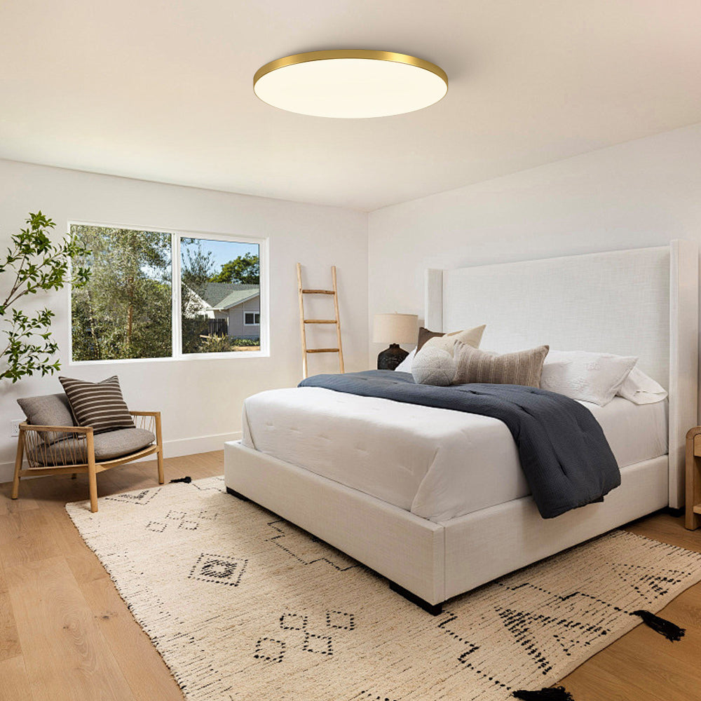Minimalist gold round LED flush mount light installed above a bed in a neutral interior
